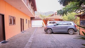 A narrow paved pathway leading to a building with a car parked on the right. - Chalés Porto Seguro (São Sebastião)