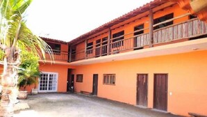 A two-story building with a balcony on the upper floor, a door on the ground floor, and a small courtyard. - Chalés Porto Seguro (São Sebastião)