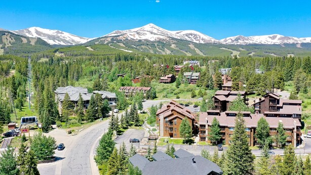 A mountain resort with multiple chalet-style buildings, a main road, and snow-capped mountains in the background. - Tyra Lookout Condo: Ski-In/Ski-Out (Breckenridge)