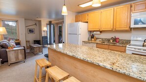 A kitchen with wooden cabinets, a granite countertop, a refrigerator, a stove, and a dining area with a bench and a table. - Tyra Lookout Condo: Ski-In/Ski-Out (Breckenridge)