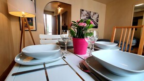 Une table à manger dressée avec de l’assiette blanche, des bols, un verre à vin et un vase rose contenant des fleurs.