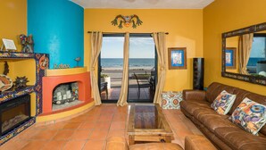 A living room with a view of the ocean, a fireplace, a sofa, and a ceiling fan.