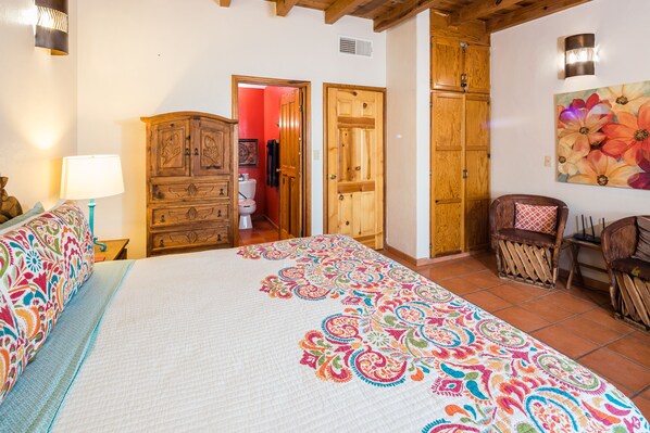 A bedroom with a large bed, wooden wardrobe, and a chair.