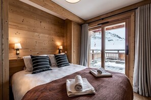 A wooden room with a bed, two lamps, and a view of a snowy landscape. - WAPA - Premium Ski-in Ski-out Apartment (Huez)