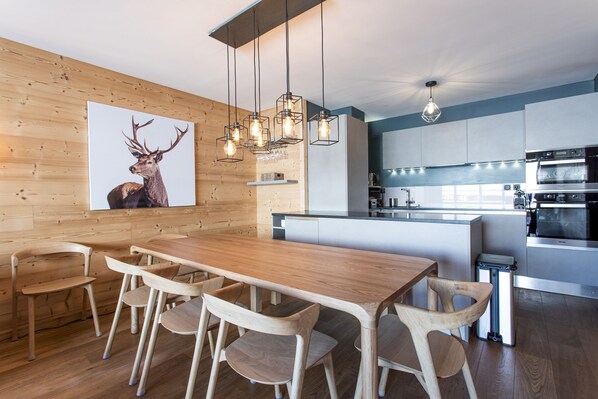 A modern kitchen with a wooden dining table and chairs, a large island, and a wall-mounted deer artwork. - WAPA - Premium Ski-in Ski-out Apartment (Huez)