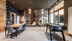 A spacious room with a foosball table, a long dining table with chairs, and a bookshelf filled with books and decorative items. - FAGUS - Spacious Apartment in Luxury Residence (Huez)