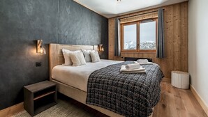 A bedroom with a large bed, a nightstand, a window with curtains, and a view of the mountains. - FAGUS - Spacious Apartment in Luxury Residence (Huez)