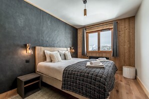 A bedroom with a large bed, a nightstand, a window with curtains, and a view of the mountains.