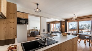 A modern kitchen with wooden cabinetry, a black sink, and a dining area with a view of snow-capped mountains. - FAGUS - Spacious Apartment in Luxury Residence (Huez)