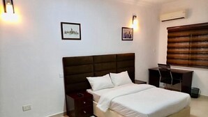 A bedroom with a large bed, a nightstand, a dresser, and two wall-mounted lights. - Esenyo Luxury Apartments (Abuja)