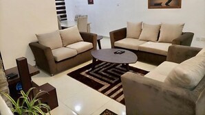 A modern living room with two sofas, a coffee table, and a rug. There is a staircase leading to another level. - Esenyo Luxury Apartments (Abuja)