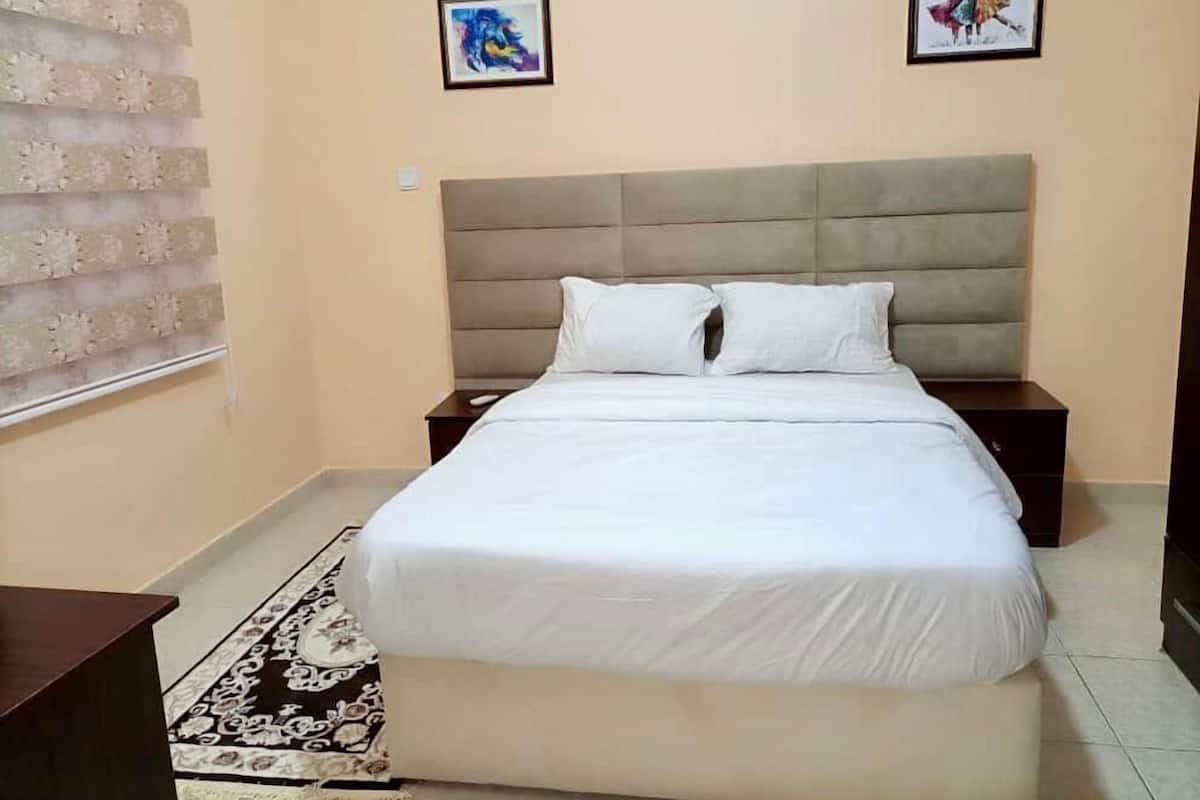 A neatly arranged bedroom with a large bed, two bedside tables, a patterned rug, and two framed pictures on the wall.