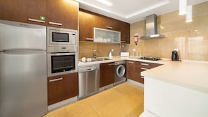 A modern kitchen with stainless steel appliances, wooden cabinets, and a large island. - Baia Residence 2 - Prata By SCH (São Martinho do Porto)