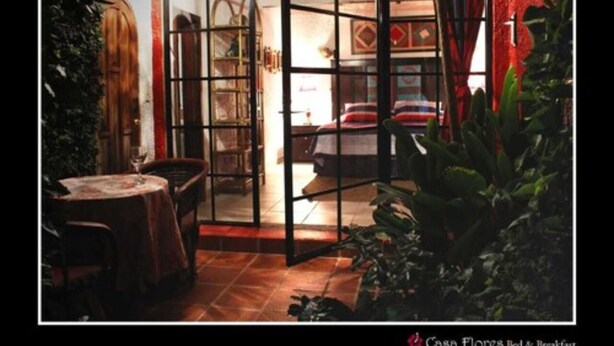 A room with a glass door leading to a dining area, a small table with a chair, and a potted plant. - Casa Flores Bed & Breakfast (Ajijic)