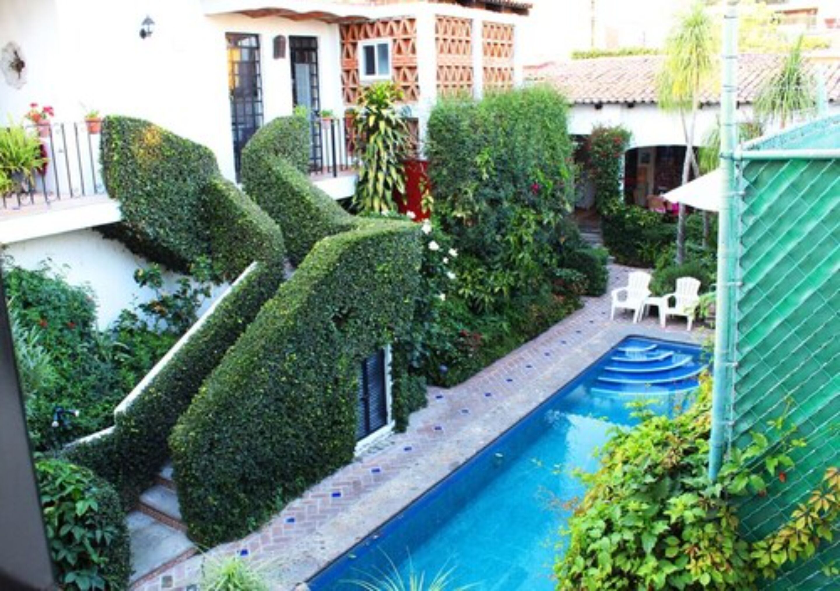 A swimming pool surrounded by neatly trimmed hedges and a brick pathway.