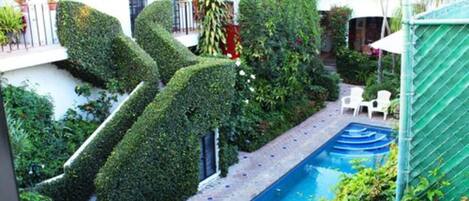 A swimming pool surrounded by neatly trimmed hedges and a brick pathway.