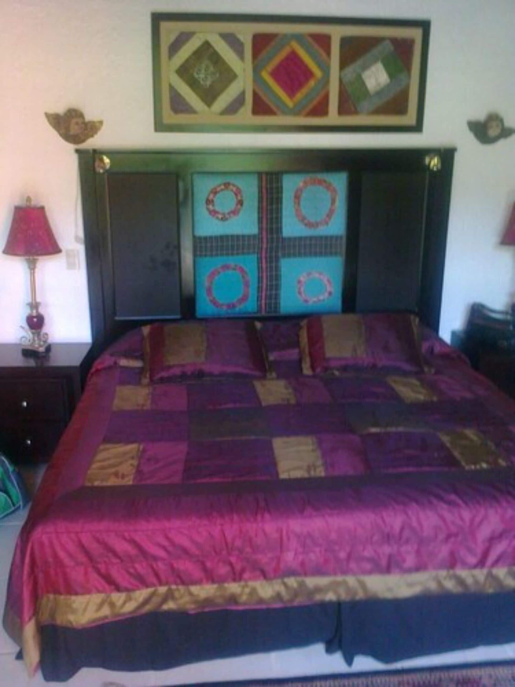 A bedroom with a bed, a nightstand, a lamp, and a wall with a framed picture.