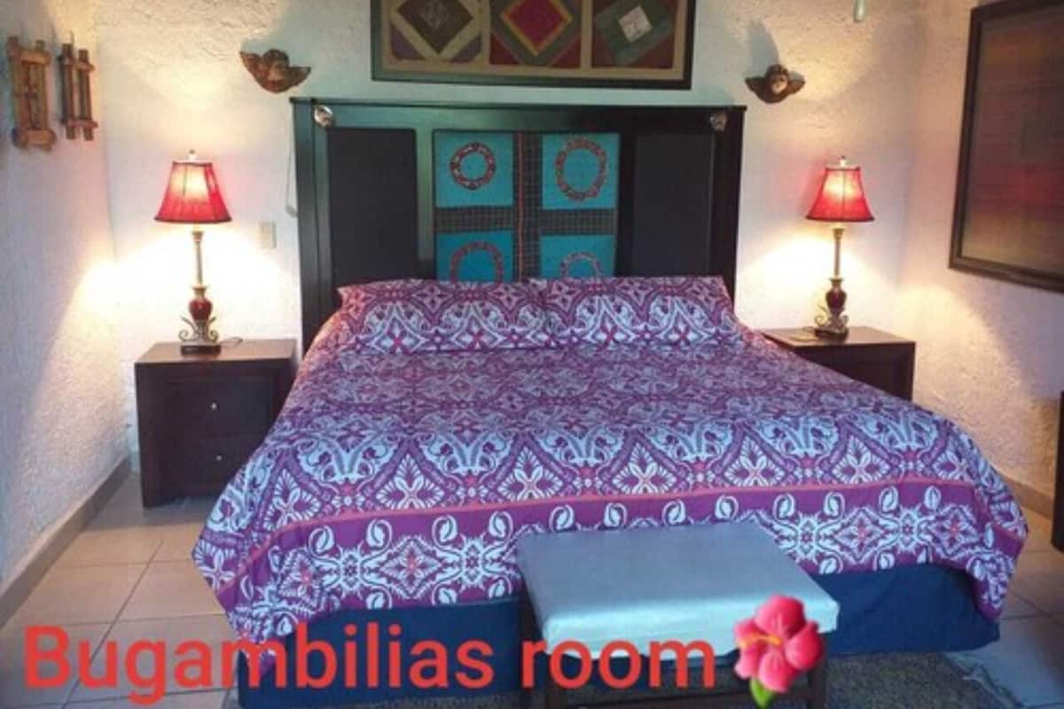 Una habitación con una cama, dos lámparas de noche, un reloj de pared y un cuadro enmarcado sobre la cama.
