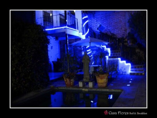 Vista nocturna de un edificio con luces de neón azules iluminadas, una estatua y una pequeña piscina.