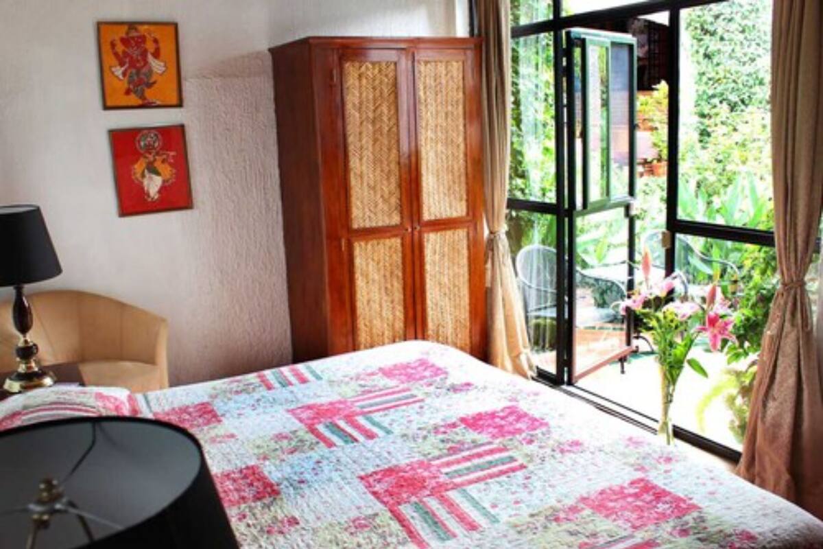 Un dormitorio con cama, escritorio, silla y armario. Hay dos cuadros en la pared y una ventana con vistas a zonas verdes.