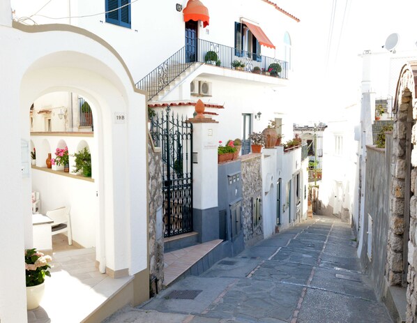 Un vicolo stretto con edifici bianchi, un balcone con piante e un cancello.