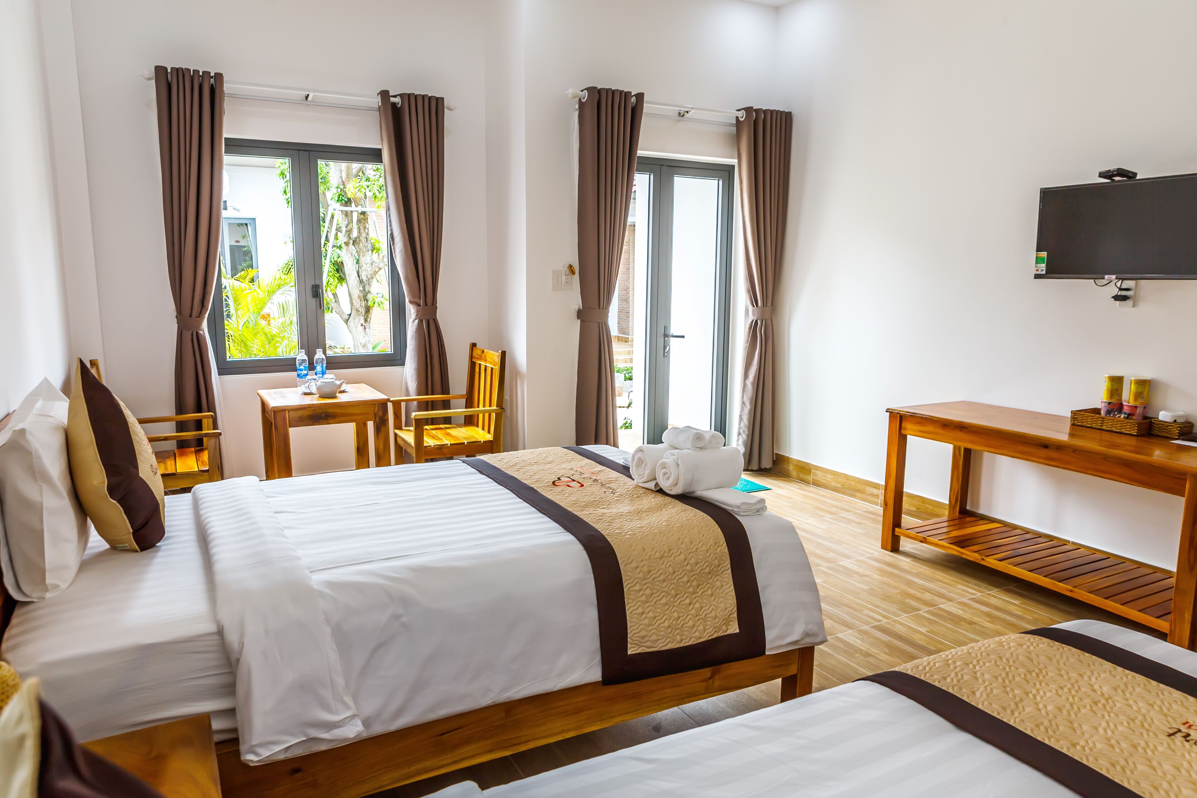 A hotel room with two beds, a desk, a chair, a TV, and a window with curtains.