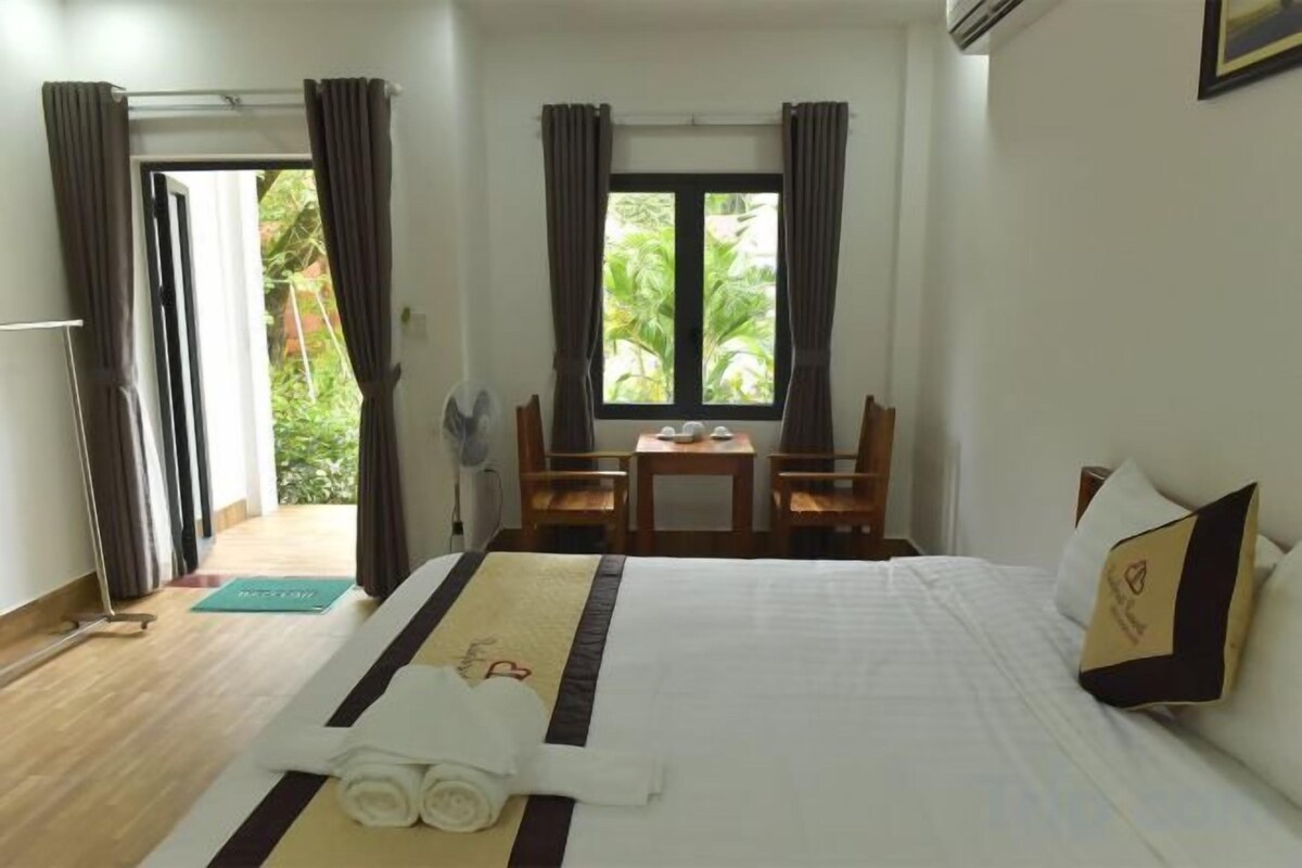 A hotel room with a bed, a table, chairs, and a view of greenery outside.