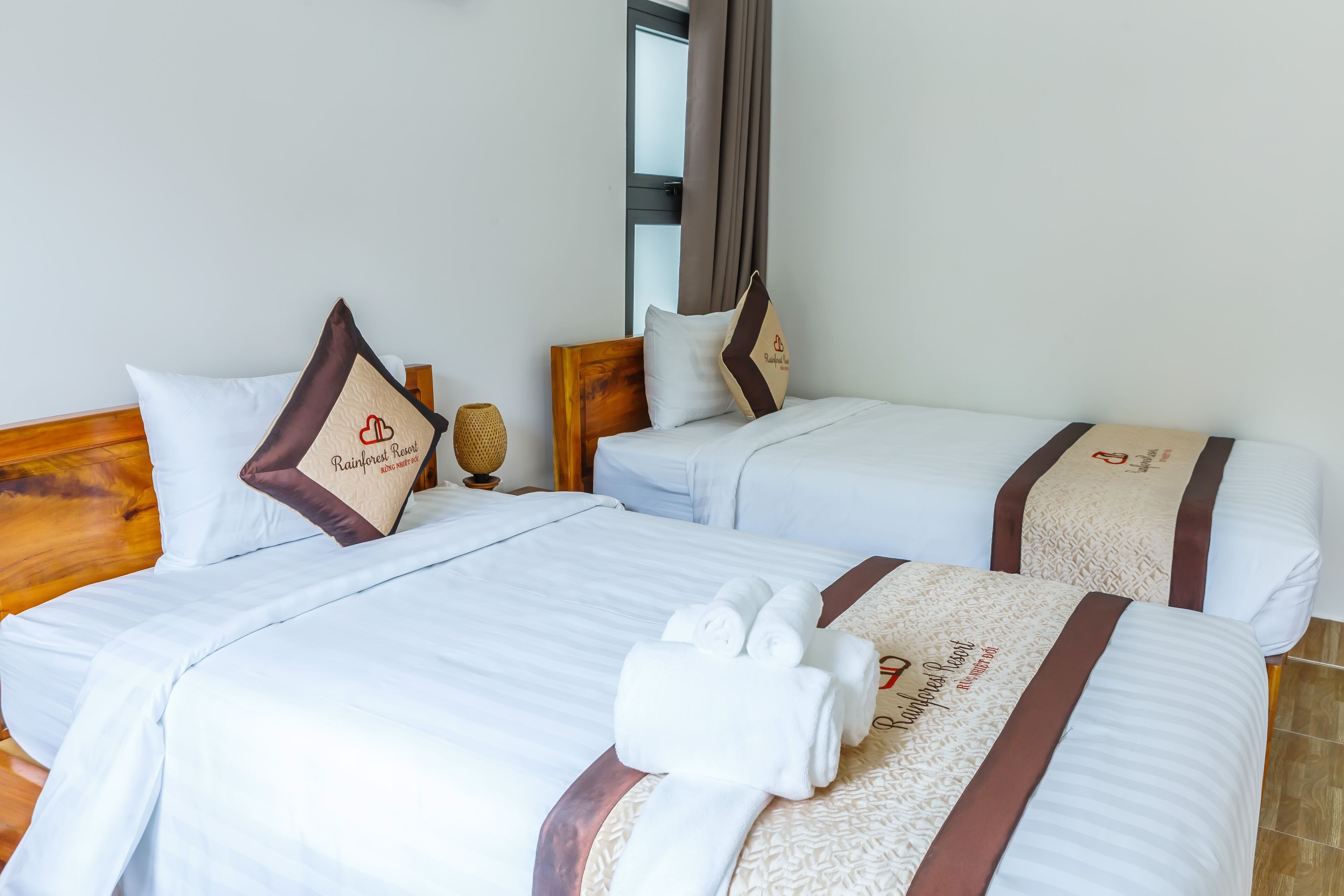 Two neatly made beds with white linens, brown headboards, and decorative pillows.