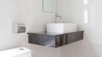 A modern bathroom with a white toilet, a stainless steel sink, and a mirror above it.