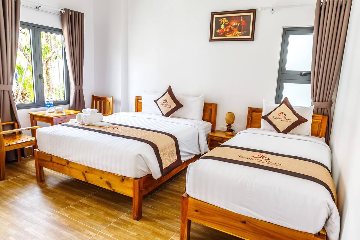 A hotel room with two wooden beds, a wooden desk, a chair, and a window with curtains.