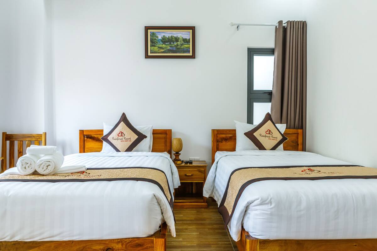 A hotel room with two beds, wooden headboards, a nightstand with a lamp, and a framed picture on the wall.
