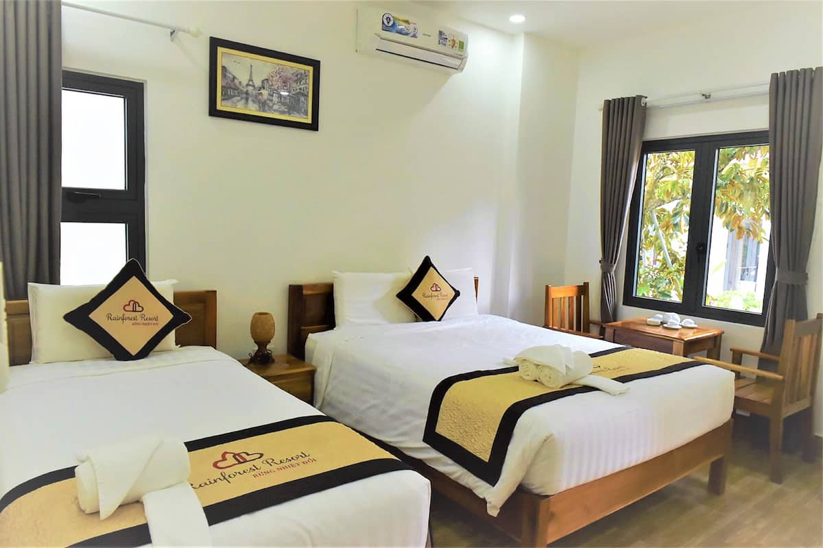 A hotel room with two beds, a small table, a chair, and a window with curtains.