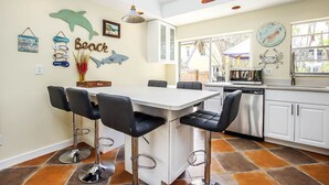 Een keuken met een wit eiland, zwarte barkrukken en een eettafel. Er hangen decoratieve wanddecoraties, waaronder een dolfijn en een krab.
