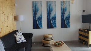 Een moderne woonkamer met een donkere bank, een rond houten poef, een houten salontafel met een mand, en drie abstracte schilderijen aan de muur.
