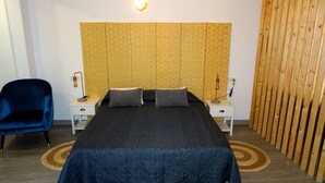 Een slaapkamer met een groot bed, twee nachtkastjes, een blauwe stoel en een wand van houten latten.