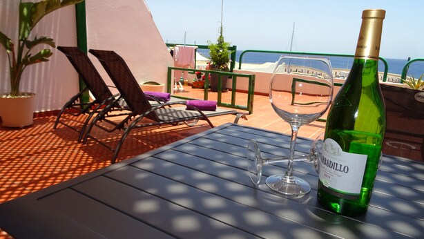Een tafel met een fles wijn en een glas op een terras met stoelen en potplanten.