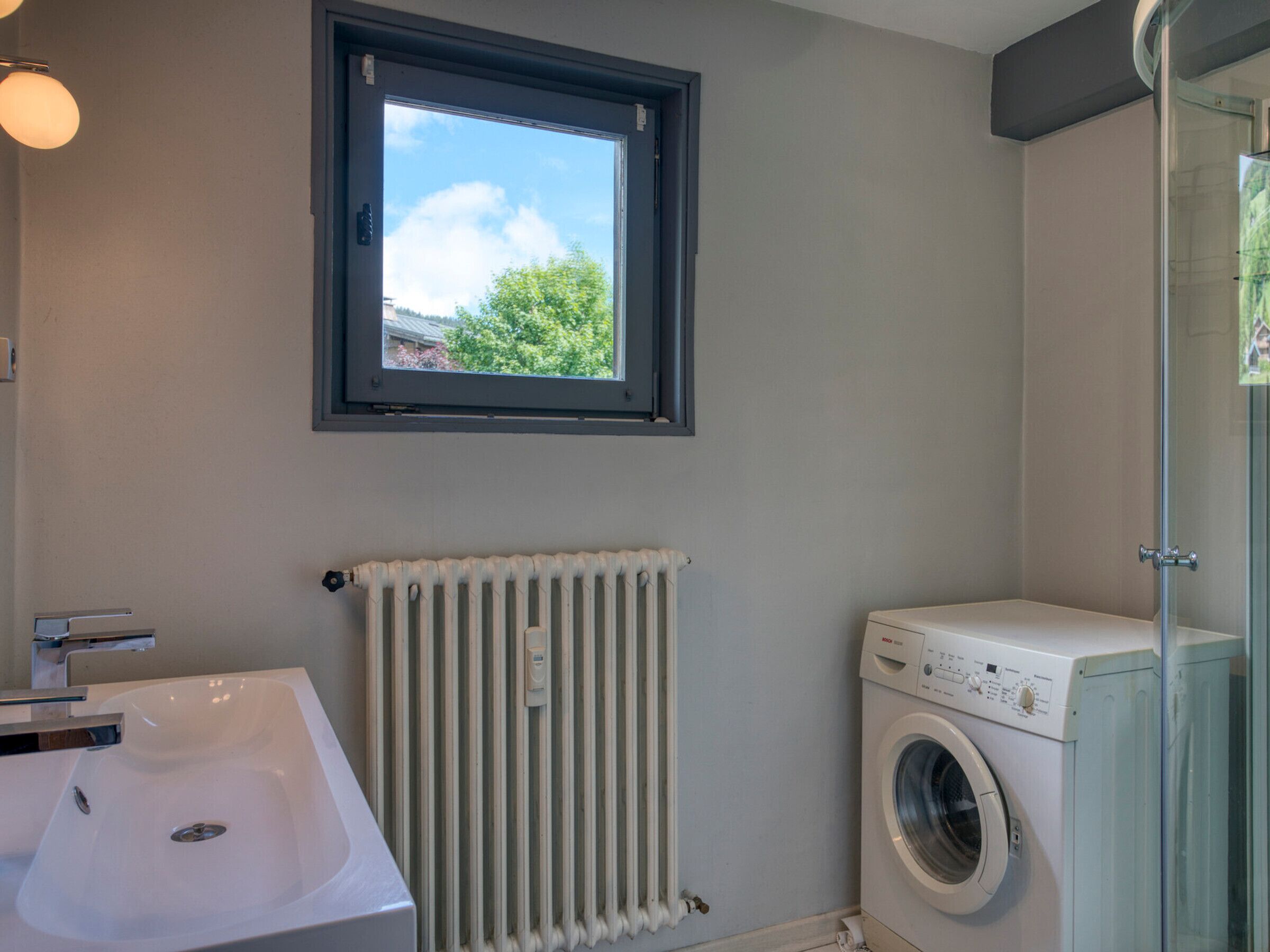 A bathroom with a white sink, a window, a radiator, and a washing machine.