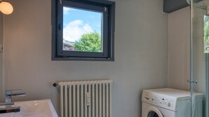 Un baño con un lavabo blanco, una ventana, un radiador y una lavadora.