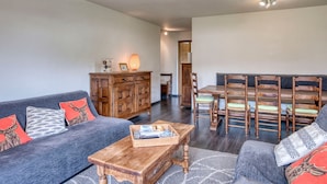 Una sala de estar acogedora con un sofá, una mesa de centro, un aparador de madera y una zona de comedor con sillas y una mesa.