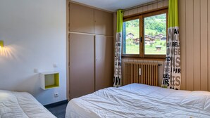 Habitación de hotel con dos camas, un armario, una ventana con cortinas y un radiador.