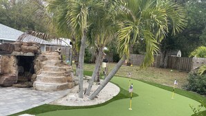 A miniature golf course with artificial grass, palm trees, and a stone structure.