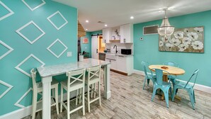 A modern kitchen with white cabinets, a marble countertop, and a dining area with a wooden table and blue chairs.