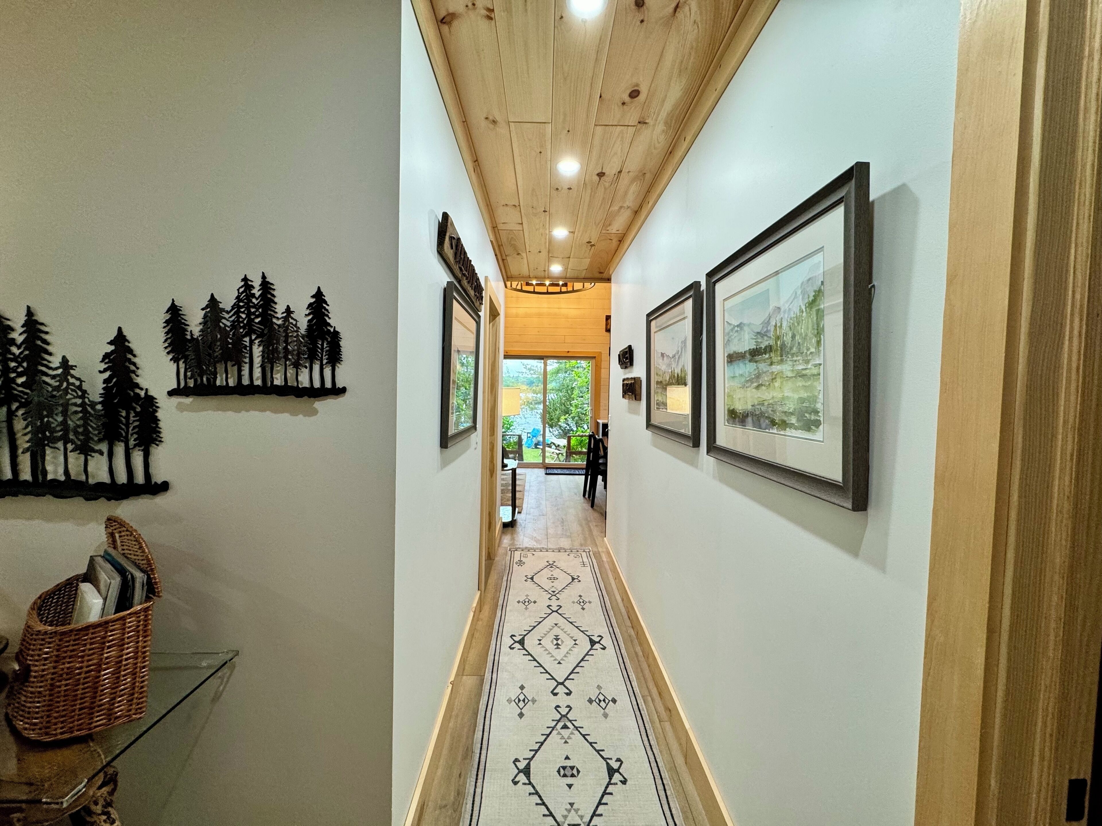 A hallway with framed artwork on the walls, a patterned rug, and a basket on a glass table.
