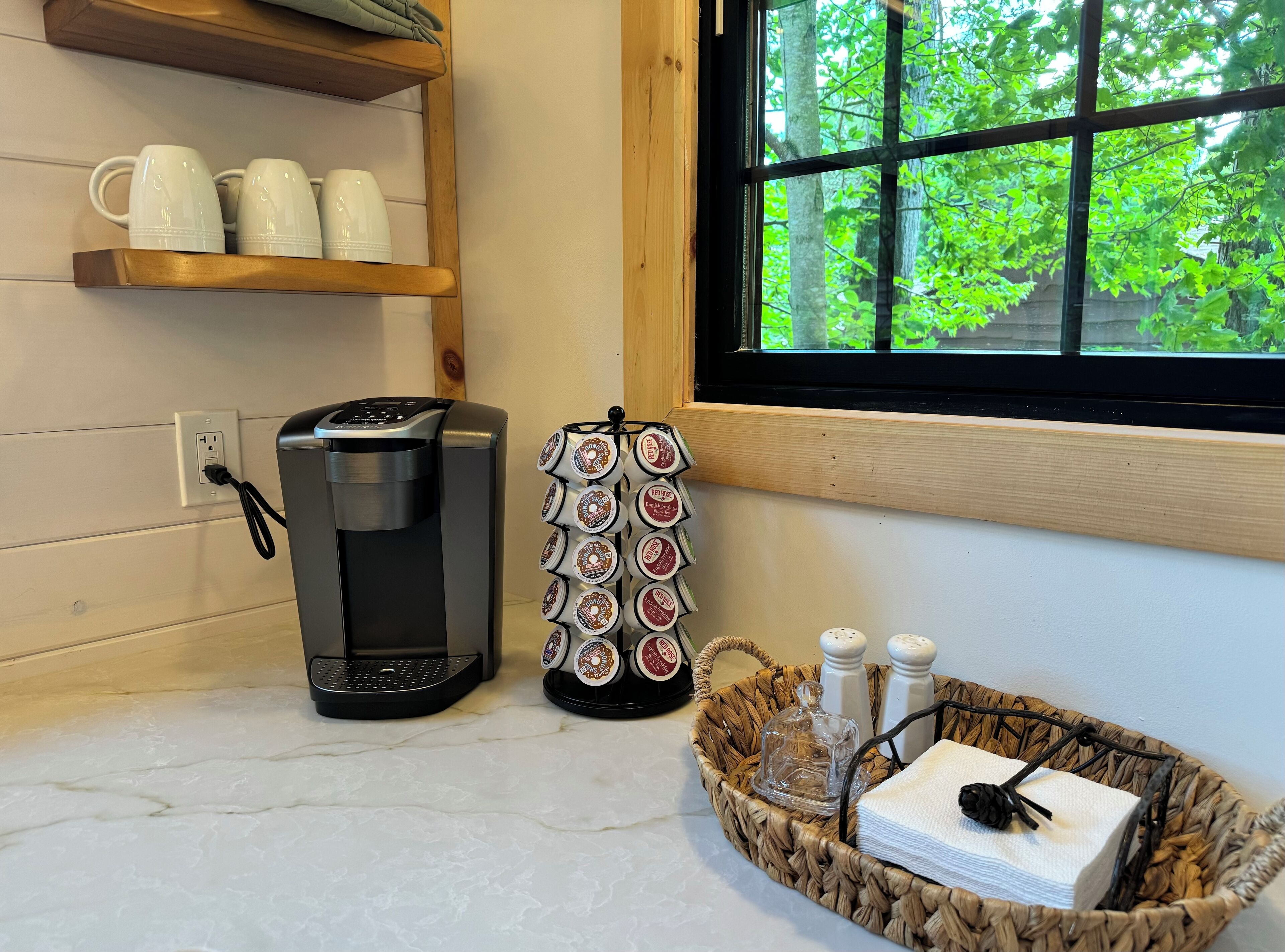 Eine Kaffeemaschine, ein Becherhalter und ein Fenster mit Blick auf Bäume.