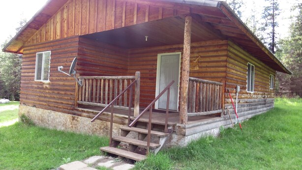 Une cabane en rondins avec une véranda, des marches en bois et une porte.