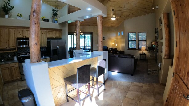 Una cocina amplia con vigas de madera, una isla central, taburetes de bar y un comedor con vistas al exterior.
