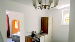 Une cuisine compacte équipée d’une cuisinière, d’un évier et de placards, qui donne sur une chambre avec un lit et une fenêtre.
