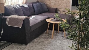A living room with a sofa, a small wooden table, a potted plant, and a brick wall. - Rajana bungalow 2(Olive House) (Ulcinj)