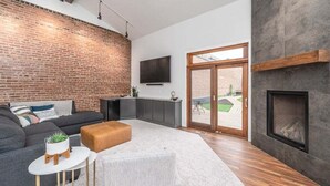 Ein modernes Wohnzimmer mit Backsteinwand, Kamin, Flachbildfernseher und großem Fenster.