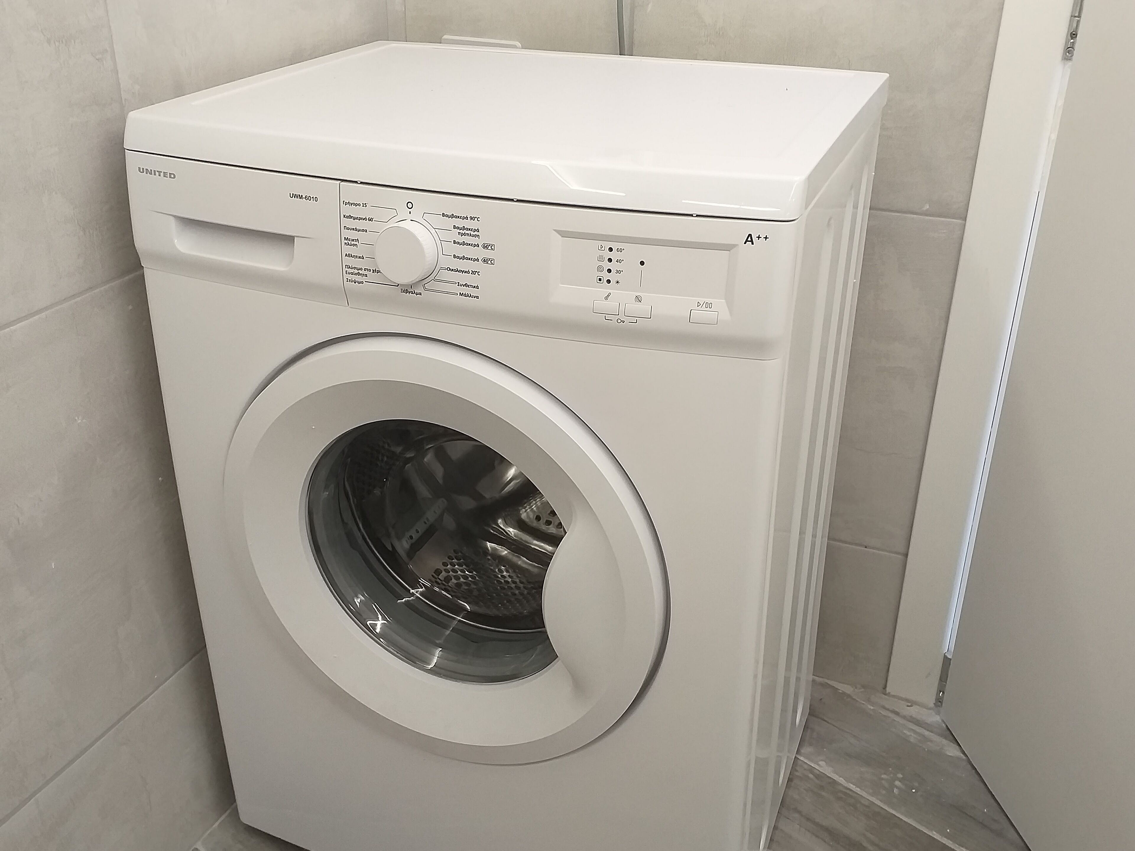 A front-loading washing machine with a control panel, located in a bathroom with tiled walls.